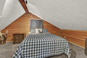 Unfurnished bedroom with vaulted ceiling, carpet, a textured ceiling, and log walls