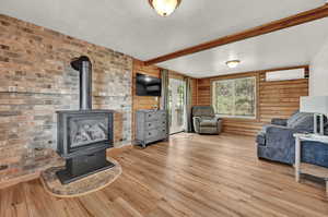 Living room with wood walls, beamed ceiling, light hardwood / wood-style flooring, and a wood stove