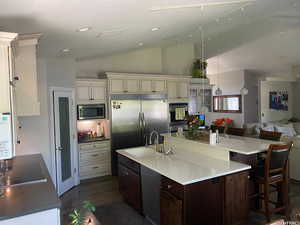 Kitchen featuring dark hardwood / wood-style flooring, a kitchen island with sink, built in appliances, vaulted ceiling, and sink