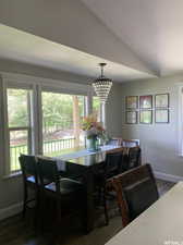 Dining area with a notable chandelier, a wealth of natural light, vaulted ceiling, and dark wood-type flooring