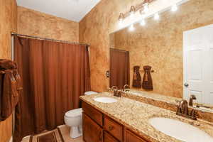 Bathroom with toilet, tile patterned floors, and dual bowl vanity