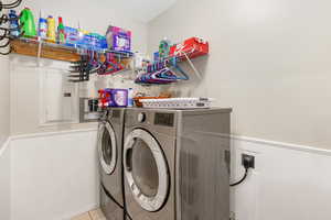 Clothes washing area featuring light tile patterned flooring, electric panel, and washing machine and dryer