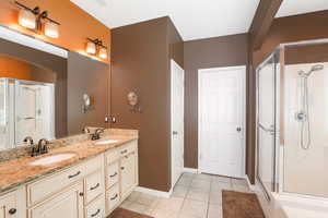 Bathroom with a shower with door, tile patterned flooring, and dual bowl vanity