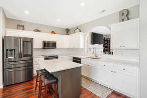 Kitchen featuring tasteful backsplash, appliances with stainless steel finishes, a kitchen island, and dark wood-type flooring