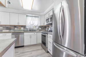 Kitchen with appliances with stainless steel finishes, white cabinetry, decorative backsplash, and sink