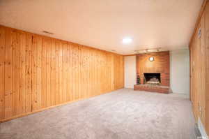 Unfurnished living room with a fireplace, brick wall, carpet flooring, wood walls, and a textured ceiling