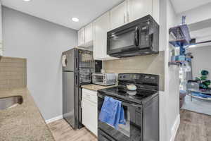 Kitchen with decorative backsplash, black appliances, light hardwood / wood-style flooring, and white cabinets