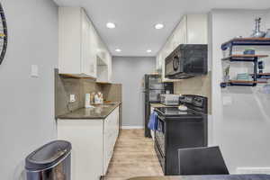 Kitchen with white cabinetry, black appliances, sink, light hardwood / wood-style flooring, and backsplash