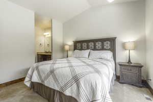 Bedroom with vaulted ceiling, sink, light carpet, and ensuite bath