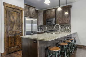 Kitchen with light stone countertops, appliances with stainless steel finishes, backsplash, dark wood-type flooring, and decorative light fixtures