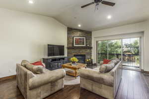 Living room featuring a fireplace, dark wood-type flooring, ceiling fan, and lofted ceiling