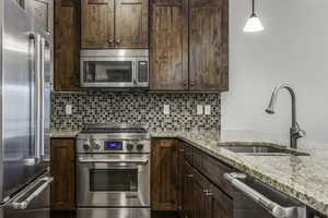 Kitchen featuring light stone countertops, hanging light fixtures, high end appliances, and sink