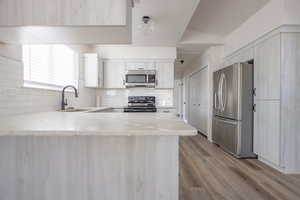 Kitchen with sink, backsplash, kitchen peninsula, light hardwood / wood-style floors, and stainless steel appliances