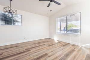 Empty room featuring light hardwood / wood-style floors, lofted ceiling, and ceiling fan with notable chandelier