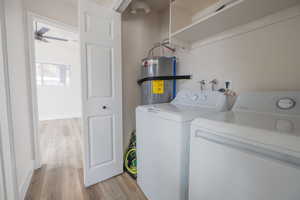 Washroom featuring light hardwood / wood-style flooring, electric water heater, washing machine and clothes dryer, and ceiling fan