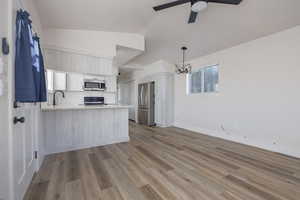 Kitchen featuring tasteful backsplash, kitchen peninsula, stainless steel appliances, vaulted ceiling, and light hardwood / wood-style flooring