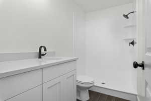 Bathroom featuring hardwood / wood-style floors, vanity, walk in shower, and toilet