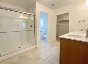 Bathroom featuring toilet, tile patterned floors, double sink vanity, and an enclosed shower