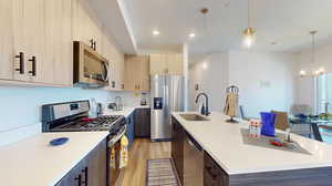 Kitchen featuring stainless steel appliances, a center island with sink, sink, pendant lighting, and light hardwood / wood-style floors