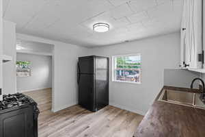 Kitchen featuring sink, black appliances, light hardwood / wood-style floors, and white cabinetry