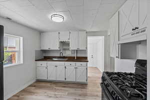 Kitchen featuring white cabinetry, gas stove, light wood-type flooring, wood counters, and sink