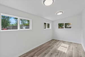 Unfurnished room featuring light wood-type flooring, lofted ceiling, and a healthy amount of sunlight