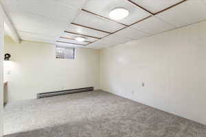 Basement with carpet floors, a paneled ceiling, and a baseboard heating unit