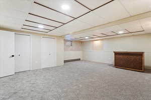 Basement featuring carpet flooring, a baseboard heating unit, and a drop ceiling