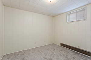 Carpeted spare room featuring a baseboard heating unit