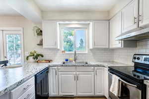 Kitchen featuring black dishwasher, electric stove, a healthy amount of sunlight, and white cabinetry