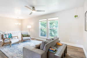 Living room featuring ceiling fan with notable chandelier and wood-type flooring