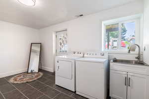 Clothes washing area with sink, cabinets, dark tile patterned flooring, and washing machine and clothes dryer