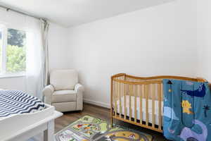 Bedroom with a crib, multiple windows, and dark hardwood / wood-style flooring