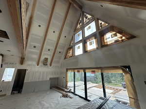 Unfurnished living room featuring high vaulted ceiling, a wealth of natural light, and beam ceiling