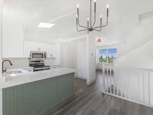 Kitchen with appliances with stainless steel finishes, white cabinets, sink, and dark wood-type flooring