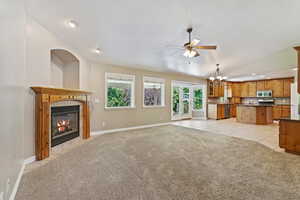 Unfurnished living room featuring lofted ceiling, ceiling fan with notable chandelier, light colored carpet, and a fireplace