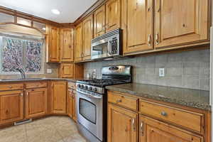 Kitchen with sink, dark stone countertops, appliances with stainless steel finishes, light tile patterned floors, and backsplash