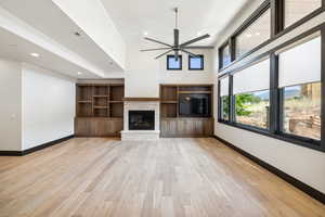 Unfurnished living room with ceiling fan, a fireplace, light hardwood / wood-style flooring, and a high ceiling