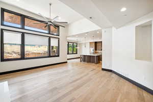 Unfurnished living room with light hardwood / wood-style flooring, ceiling fan, and a towering ceiling