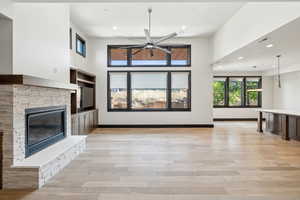 Unfurnished living room featuring a stone fireplace, a towering ceiling, light hardwood / wood-style flooring, and ceiling fan