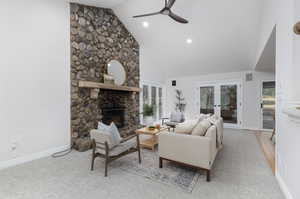 Carpeted living room with a stone fireplace, french doors, ceiling fan, and high vaulted ceiling