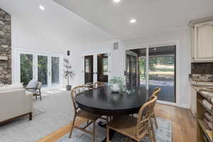 Dining space featuring a healthy amount of sunlight, french doors, light hardwood / wood-style flooring, and vaulted ceiling