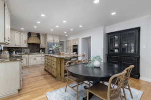 Kitchen with light hardwood / wood-style floors, custom exhaust hood, appliances with stainless steel finishes, and a kitchen island