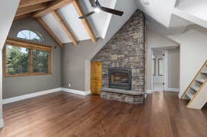 Unfurnished living room featuring beamed ceiling, hardwood / wood-style flooring, a fireplace, high vaulted ceiling, and ceiling fan