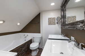 Bathroom with dual vanity, tiled bath, lofted ceiling, tile patterned floors, and toilet