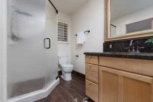 Bathroom featuring a shower with shower door, vanity, hardwood / wood-style floors, and toilet