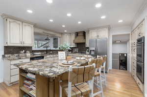 Kitchen featuring decorative backsplash, stainless steel appliances, custom exhaust hood, and light wood-type flooring