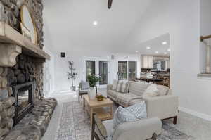 Carpeted living room with a stone fireplace, sink, and high vaulted ceiling