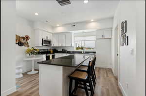 Kitchen featuring a kitchen bar, a center island, stainless steel appliances, white cabinetry, and light wood-type flooring