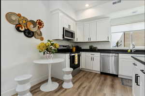 Kitchen with light wood-type flooring, appliances with stainless steel finishes, white cabinetry, and sink